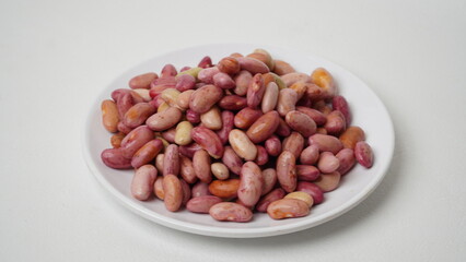 A collection of raw red beans placed on a white plate with a white base and background (isolated white).