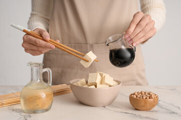 Woman with bowl of tasty tofu cheese and sauce on table
