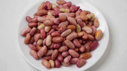 A collection of raw red beans placed on a white plate with a white base and background (isolated white).