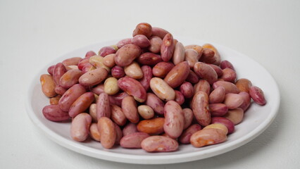 A collection of raw red beans placed on a white plate with a white base and background (isolated white).