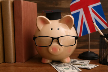 Piggy bank with money, books and UK flag on wooden table, closeup. Student loan concept
