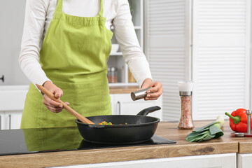 Young woman adding salt in roasted vegetables in kitchen