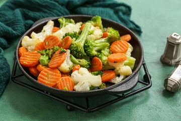 Frying pan with roasted vegetables on green background, closeup