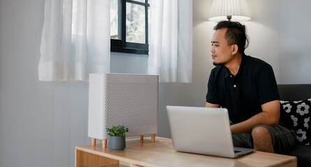 Air purifier in a living room, man working with laptop with filter for clean room 
