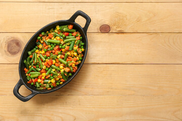 Frying pan with tasty roasted vegetables on wooden background