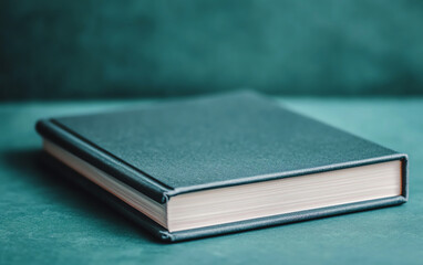 Close-up of closed book with teal hardcover on matching background, emphasizing minimalistic design.