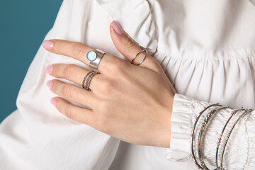 Pretty young woman in stylish white blouse with silver rings and bracelets on dark turquoise background, closeup