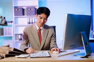 Asian Businessman analyzing reports in a modern office, working on a computer. Perfect for...