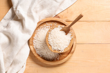 Tray and bowl of raw rice with scoop on wooden background