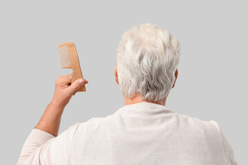Senior man with hair loss problem holding comb on grey background, back view