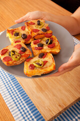 Caucasian person with fair skin holding tasty pizza pieces in gray plate on blue napkin and bamboo cutting board,