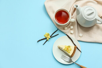 Plate of sweet cheesecake slice with vanilla flowers and cup of tea on blue background