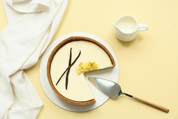 Cut sweet vanilla cheesecake with vanilla flowers and sticks on yellow background