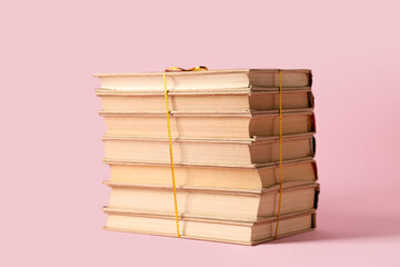 Stack of books with golden ribbon on pink background