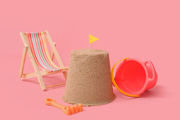 Beautiful sand castle with flag, mini deckchair and beach toys on pink background