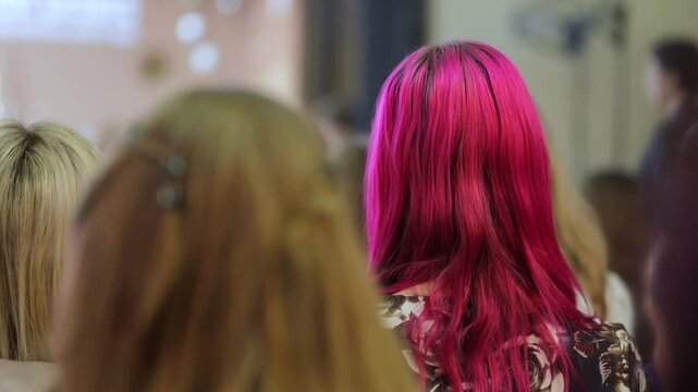 A group of women with different hair colors, one of them with pink hair. The women are sitting together and looking at something