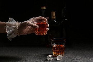 Young woman in mesh gloves holding glass of cold rum on dark background