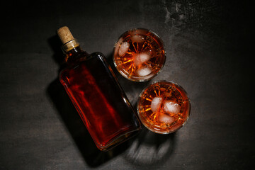 Bottle and glasses of cold rum on black grunge background
