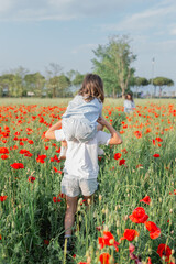 rear view of bigger child carrying on shoulders smaller one walking in a poppy field