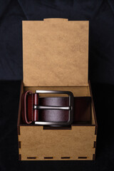 brown leather belt in brown wooden gift box on dark background, close-up