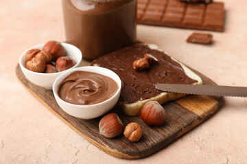 Wooden board of toast with sweet chocolate spread and hazelnuts on beige background