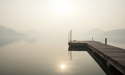 Obraz premium A single wooden pier extending into a calm lake, surrounded by soft fog and muted pastel tones.
