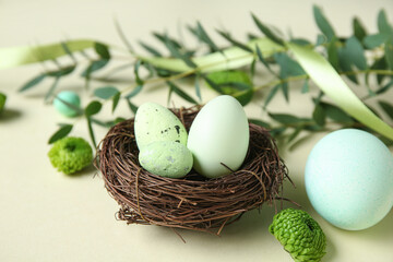 Easter eggs, decorative nest, green twigs and flowers on beige background, closeup