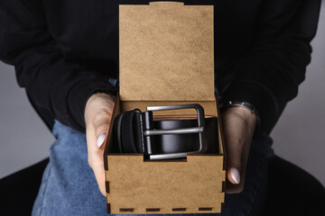 girl is holding black leather belt in brown wooden gift box, close-up