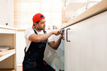 Professional handyman in uniform installing a kitchen cabinet handle. Home repair, renovation, and...