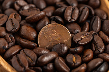 A U.S. penny among roasted coffee beans in a wooden bowl. Concept of value, economy, and coffee culture.