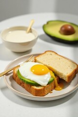 A delicious open-faced sandwich featuring a perfectly fried egg and avocado slices on toasted bread, accompanied by a bowl of creamy sauce