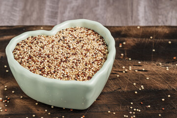 Heart-shaped ceramic bowl filled with mixed quinoa grains on a rustic wooden background. Concept of healthy eating and nutrition.