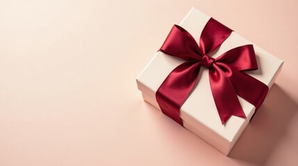 A delicately wrapped gift box, adorned with a rich burgundy ribbon, rests on a soft blush background, ready for a special occasion