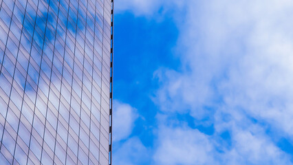 A reflective glass building occupies the left, showcasing a grid pattern and subtle sky reflections. To the right, a vibrant blue sky with scattered clouds adds contrast.