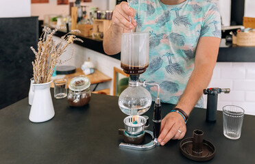 Unrecognizable barista expertly stirring with spoon a specialty coffee into siphon of Japanese coffee maker in modern cafe setting, focusing on the art of beverage preparation.