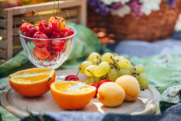 Bright fresh fruits and berries laid out on a summer picnic blanket. Cherries, grapes, and juicy oranges against