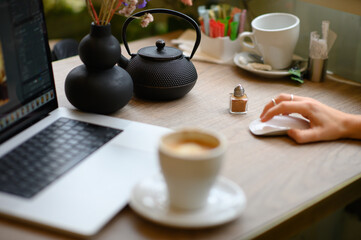 A woman works on her laptop in a café, sipping coffee. The cozy atmosphere and soft lighting create a productive yet relaxed environment for her to focus and enjoy her beverage.