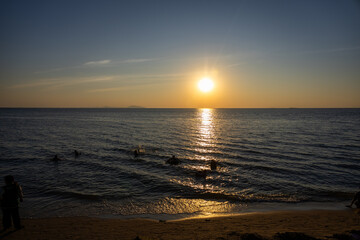 breathtaking sunset over a calm ocean, with the sun casting golden reflections on the water and silhouettes of people enjoying