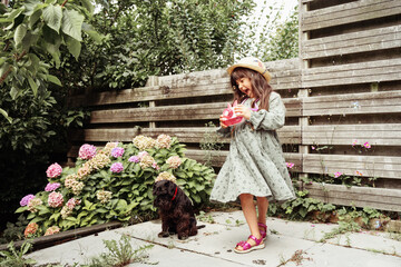 Little girl blowing soap bubbles with a dog in garden