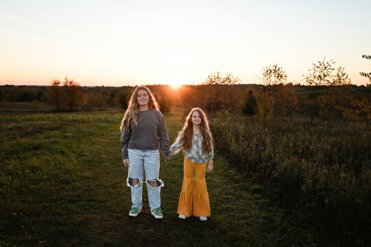Beautiful sisters holding hands smiling under sunny sky