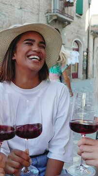 Vertical HD video of young happy diverse women friends enjoying time together toasting red wine and eating Italian aperitif in a restaurant. Friendship concept.