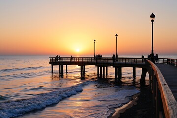Fototapeta premium Wooden pier with people watching a vibrant orange sunset over ocean waves, tranquil coastal landscape
