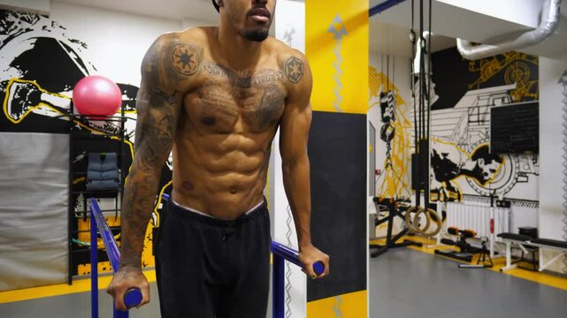 Strong black guy training abdominal muscles on parallel bars at gym. Afro american sportsman exercising at sport club. Muscular african athlete working out at fitness centre. Healthy lifestyle concept
