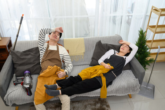 Tired couple lays back on the couch, overwhelmed after tidying up their home