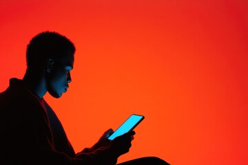 Silhouette of person engaging with phone against vibrant orange