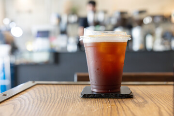 A cup of coffee sits on a coaster on a wooden table. ice americano coffee in plastic cup.