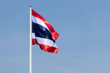A red, white and blue flag with a white stripe. Thai Flag blowing on blue sky.