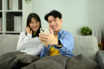 Happy couple relaxing on the sofa and using a smartphone to take a selfie or video call