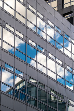 Glass facade of a contemporary building reflecting dynamic cloud formations, creating a striking urban composition of geometry and light.