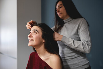 Fototapeta premium Mother braiding teenage daughter's hair at home